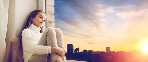 Image showing sad girl sitting on sill at home window