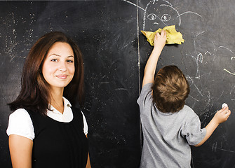 Image showing little cute boy in glasses with young real teacher, classroom studying at blackboard school kido