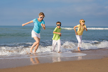 Image showing Three happy children running on the beach at the day time.