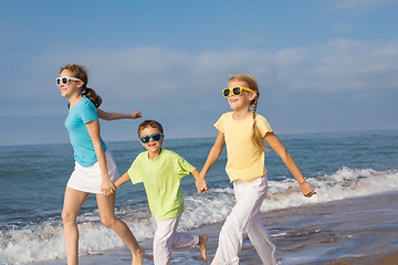 Image showing Three happy children running on the beach at the day time.