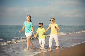 Image showing Three happy children running on the beach at the day time.