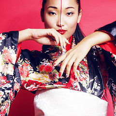 Image showing young pretty geisha on red background posing in kimono, oriental people concept 