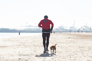 Image showing Senior Man Exercising On Beach With His Dog Running Next To Him.