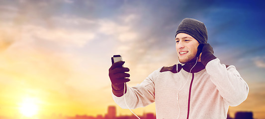 Image showing happy man with earphones and smartphone in winter