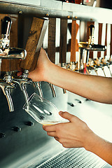 Image showing Hand of bartender pouring a large lager beer in tap.