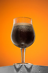 Image showing glass of cold frothy dark beer on an old wooden table