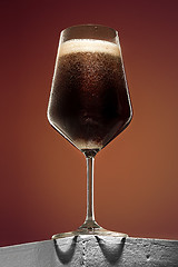 Image showing glass of cold frothy dark beer on an old wooden table