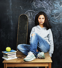 Image showing young cute teenage girl in classroom at blackboard seating on ta