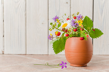 Image showing Ripe strawberries and a bouquet of forest flowers in a clay mug