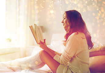 Image showing happy young woman reading book in bed at home