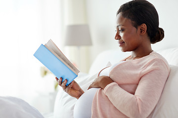 Image showing happy pregnant african woman reading book at home