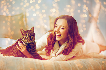 Image showing happy young woman with cat lying in bed at home