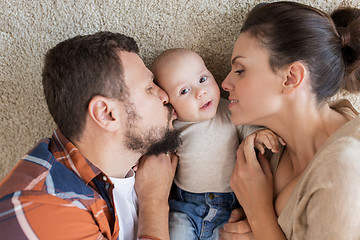 Image showing happy family lying on floor and kissing their baby