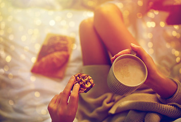 Image showing close up of woman with cocoa cup and cookie in bed