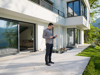 Image showing man using mobile phone in front of his luxury home villa