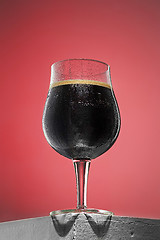 Image showing glass of cold frothy dark beer on an old wooden table