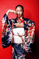 Image showing young pretty geisha on red background posing in kimono, oriental people concept close up