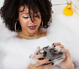 Image showing young afro-american teen girl laying in bath with foam, wearing swag jewelry flawless, making selfie, modern lifestyle concept