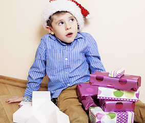 Image showing little cute boy with Christmas gifts at home. close up emotional face on boxes in santas red hat