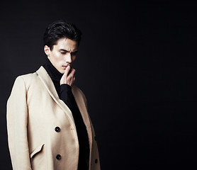 Image showing cool real young handsome fashion style man in coat on black background posing, thinking, lifestyle people concept