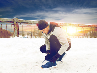 Image showing man with earphones tying sports shoes in winter