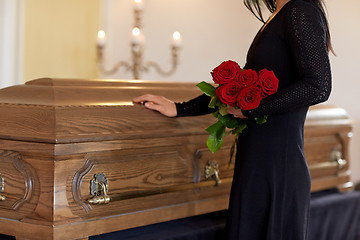 Image showing sad woman with red roses and coffin at funeral