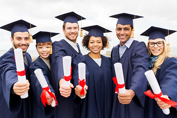 Image showing happy students in mortar boards with diplomas