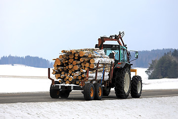 Image showing Farm Tractor Transports Logs on Wood Trailer