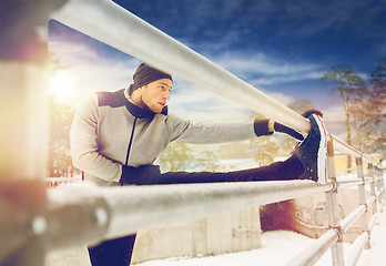 Image showing sports man stretching leg at fence in winter