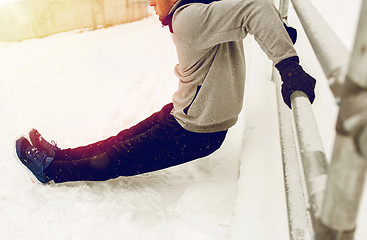 Image showing sports man doing triceps dips at fence in winter