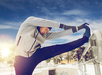 Image showing sports man stretching leg at fence in winter