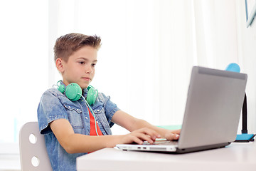 Image showing happy boy with headphones typing on laptop at home