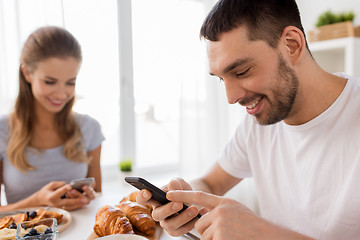 Image showing couple with smartphones having breakfast at home