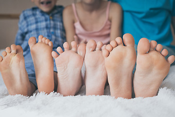 Image showing Happy brother and sisters  sitting on the bed barefoot