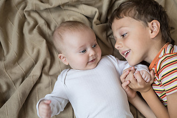 Image showing little boy playing with newborn on the bed