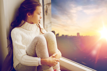 Image showing sad girl sitting on sill at home window