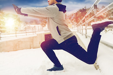 Image showing sports man stretching leg at fence in winter