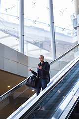 Image showing Businesswoman with large black bag and mobile phone descending on escalator.