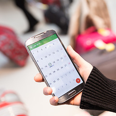 Image showing Woman checking calendar information on mobile phone sitting in airport terminal.