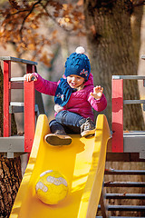 Image showing Happy three-year baby girl in jacket on slide