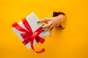 Image showing close-up of female hand holding a present through a torn paper, isolated