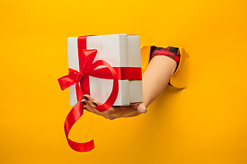 Image showing close-up of female hand holding a present through a torn paper, isolated