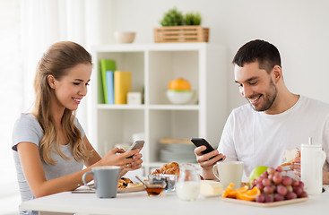 Image showing couple with smartphones having breakfast at home