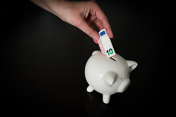 Image showing Woman putting a ten Euro bank note into a piggy bank