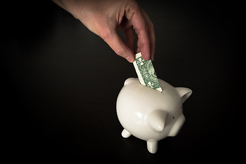 Image showing Woman putting a US Dollar bank note into a piggy bank