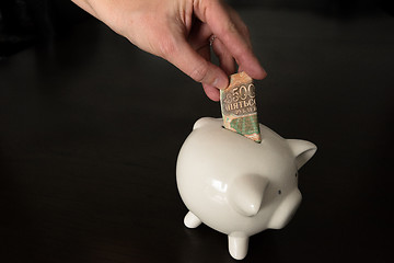 Image showing Woman putting a 500 Russian Rubles bank note into a piggy bank