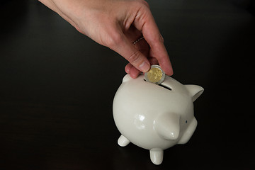 Image showing Woman putting two Euro coin into a piggy bank