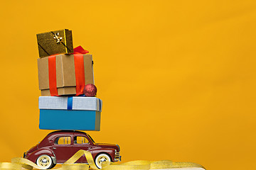 Image showing Blue retro toy car delivering Christmas or New Year gifts, on yellow