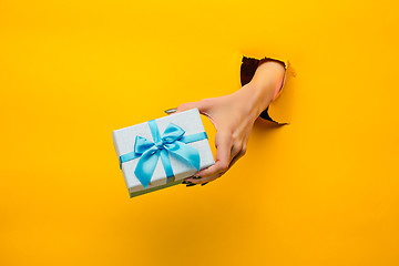 Image showing close-up of female hand holding a present through a torn paper, isolated