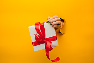 Image showing close-up of female hand holding a present through a torn paper, isolated